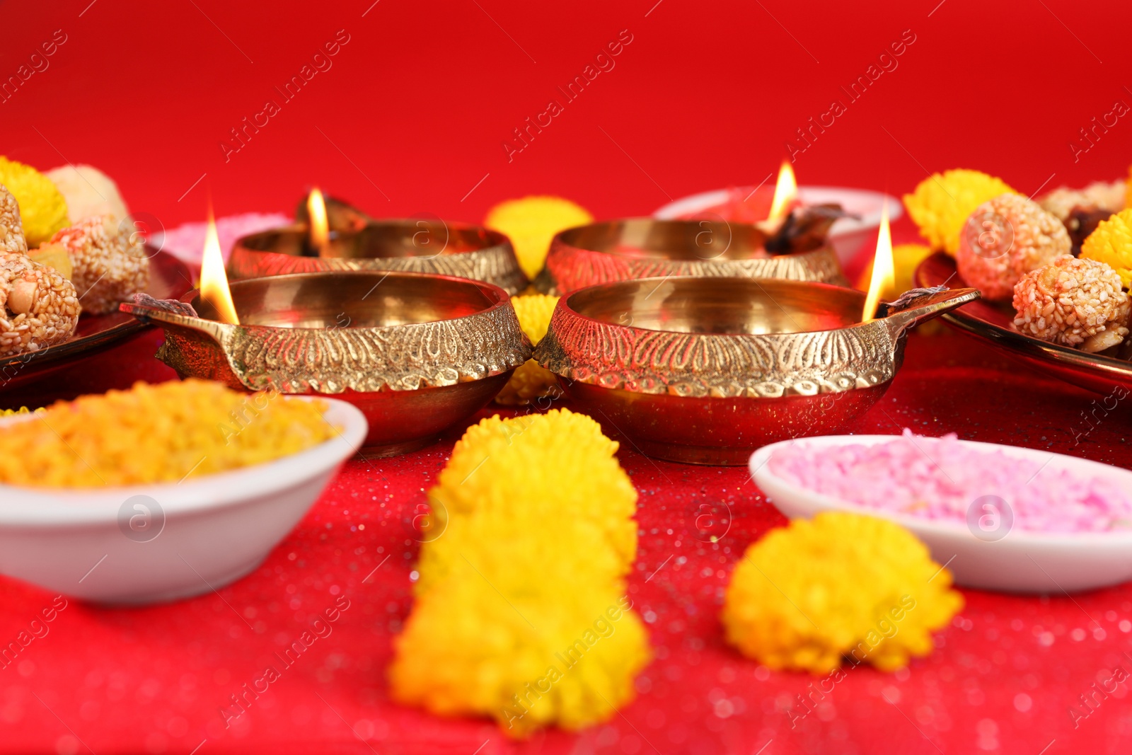 Photo of Diwali celebration. Diya lamps and bright rangoli on shiny red table, closeup