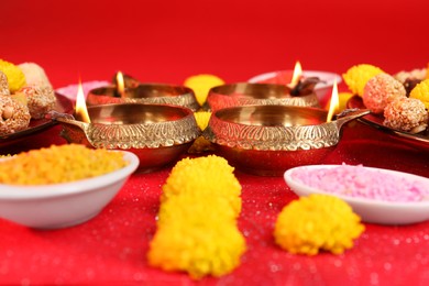Photo of Diwali celebration. Diya lamps and bright rangoli on shiny red table, closeup