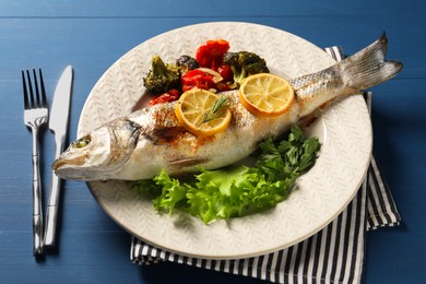 Photo of Delicious baked fish and vegetables served on blue wooden table