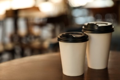 Photo of Cardboard takeaway coffee cups with plastic lids on wooden table in outdoor cafe, space for text