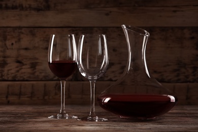 Elegant decanter with red wine and glasses on wooden table