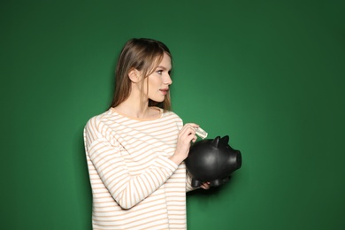 Young woman putting money into piggy bank on color background. Space for text