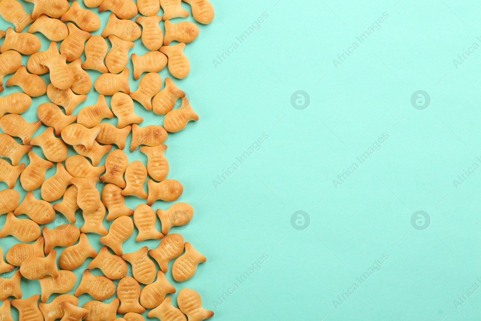 Photo of Delicious goldfish crackers on turquoise background, flat lay. Space for text