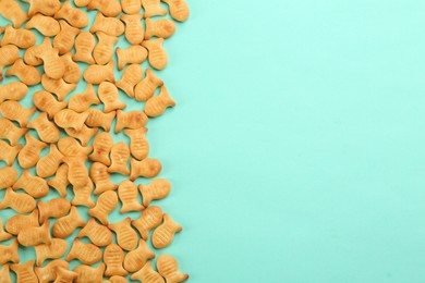 Photo of Delicious goldfish crackers on turquoise background, flat lay. Space for text