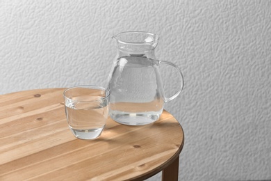 Photo of Pitcher and glass with water on table near white wall. Space for text