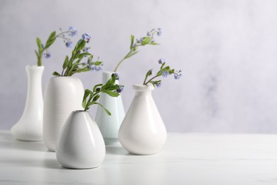 Photo of Beautiful forget-me-not flowers in vases on white marble table, closeup. Space for text