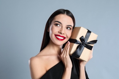 Woman in black dress holding Christmas gift on grey background