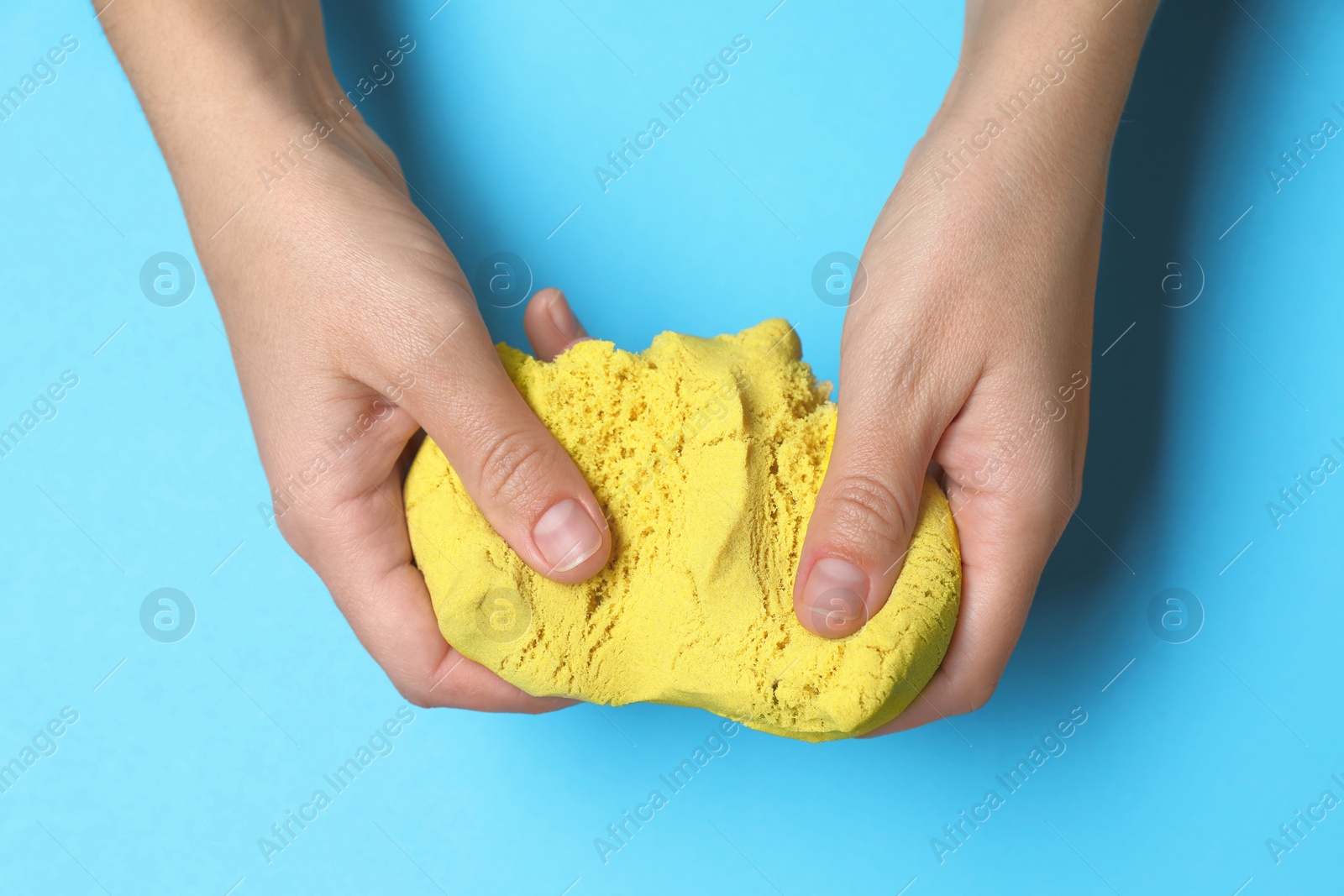 Photo of Woman playing with yellow kinetic sand on light blue background, top view