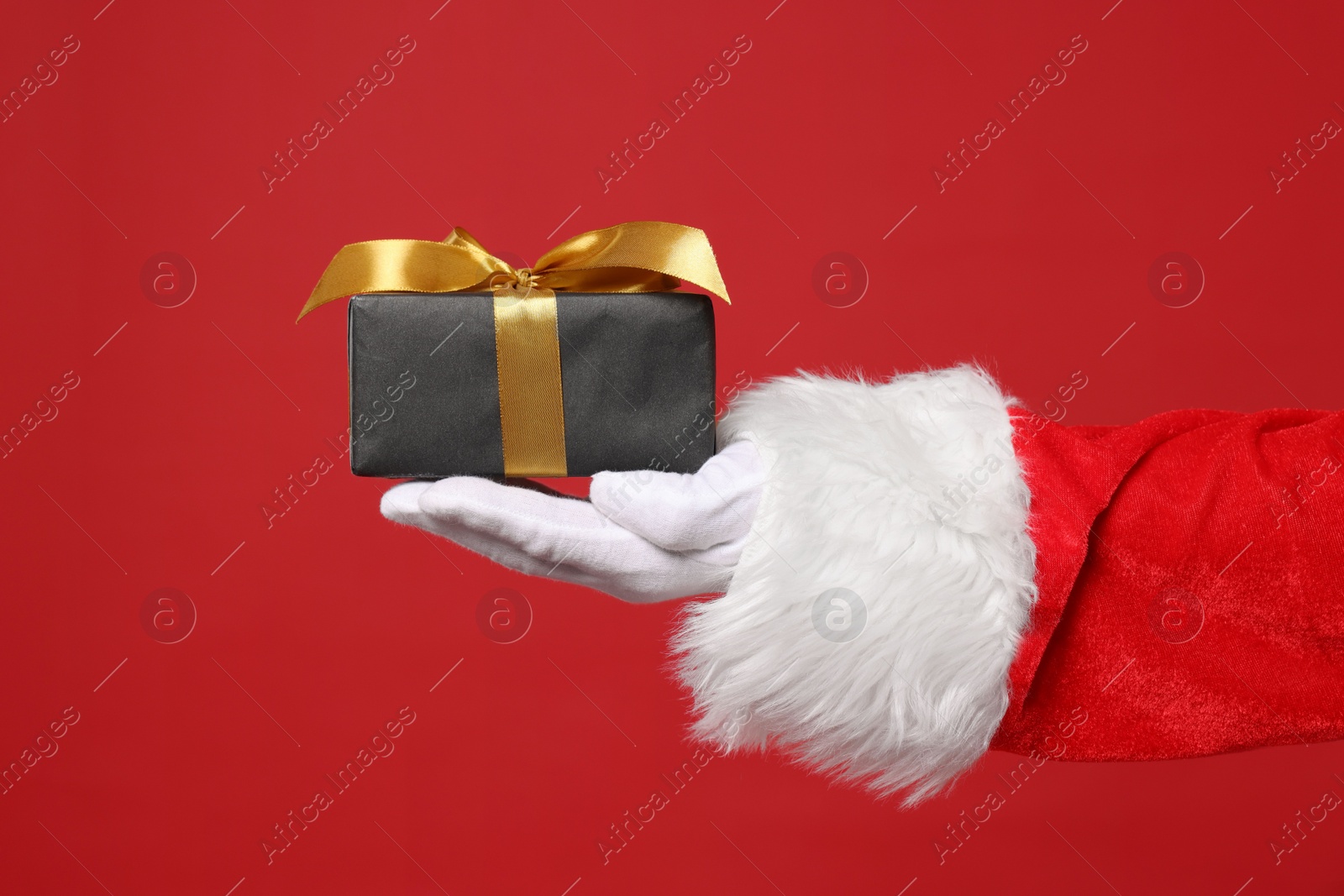 Photo of Santa Claus holding Christmas gift on red background, closeup