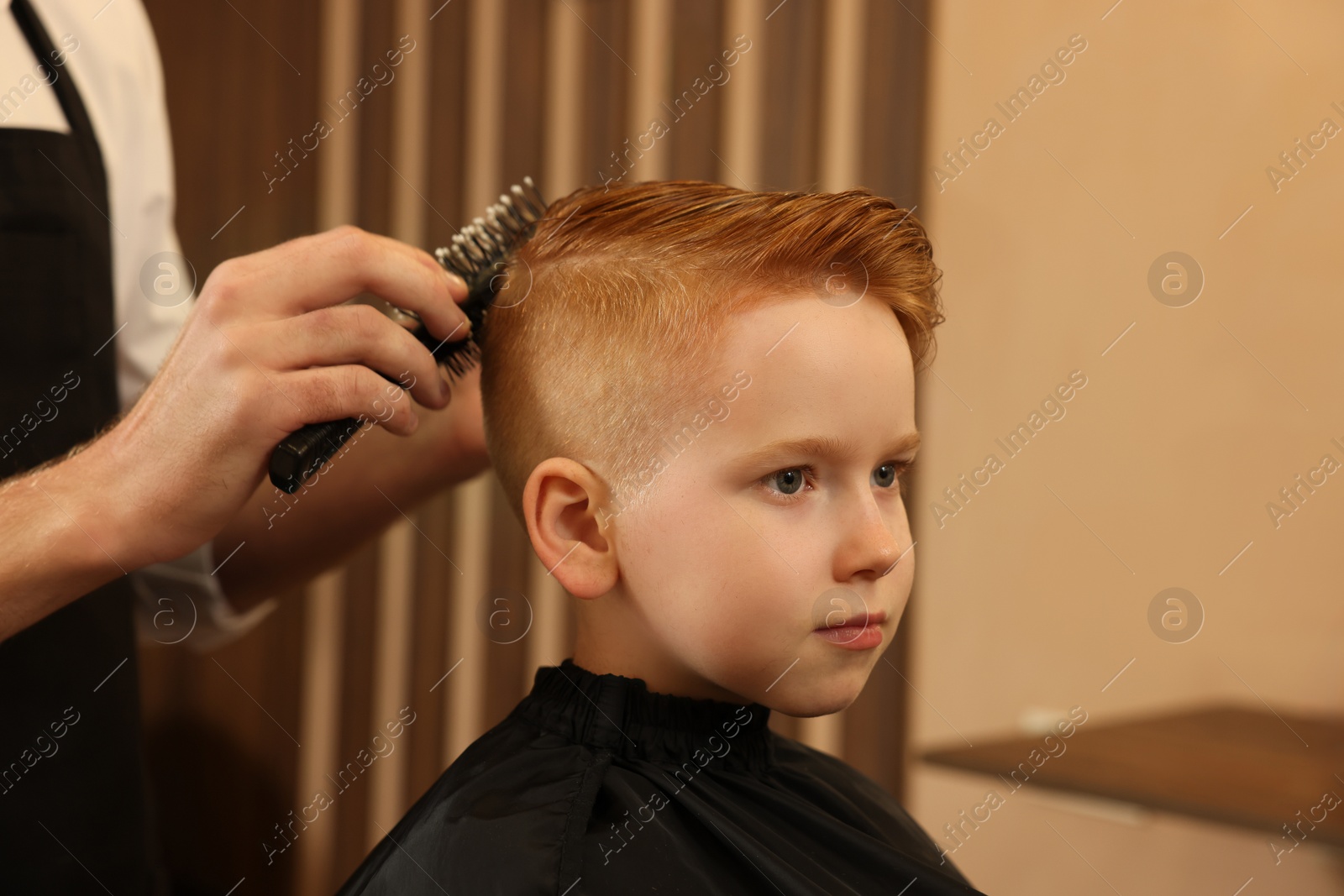 Photo of Professional hairdresser brushing boy's hair in beauty salon, closeup