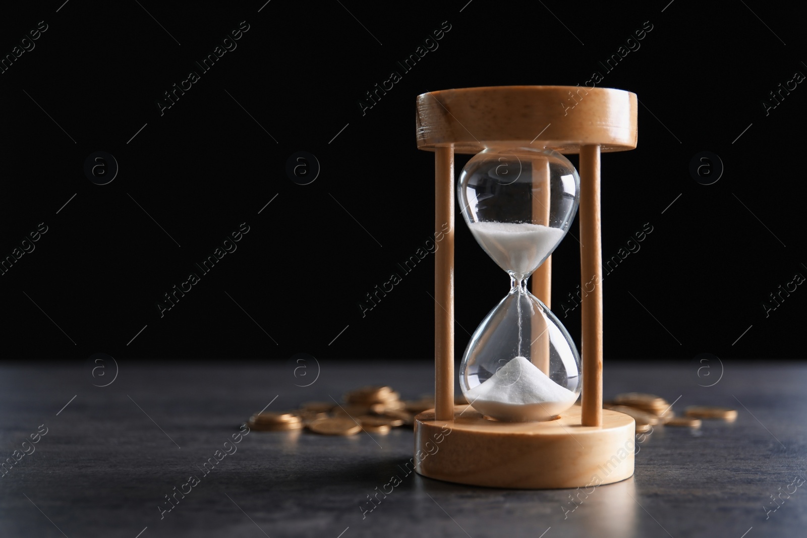 Photo of Hourglass and coins on table against black background. Time management