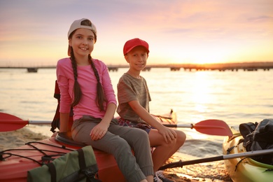 Photo of Happy children sitting on kayak near river at sunset. Summer camp