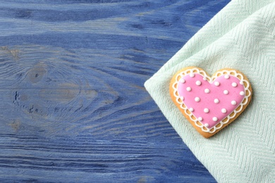 Decorated heart shaped cookie with napkin and space for text on wooden background, top view