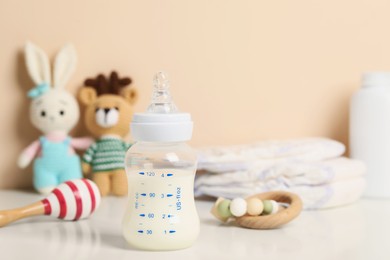 Photo of Feeding bottle with milk and other baby accessories on white table near beige wall. Space for text