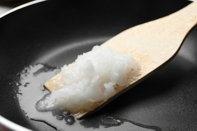 Photo of Frying pan with coconut oil and wooden spatula, closeup. Healthy cooking