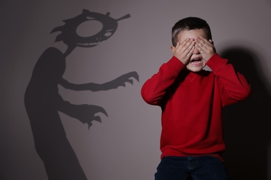 Image of Shadow of monster and scared little boy on beige background