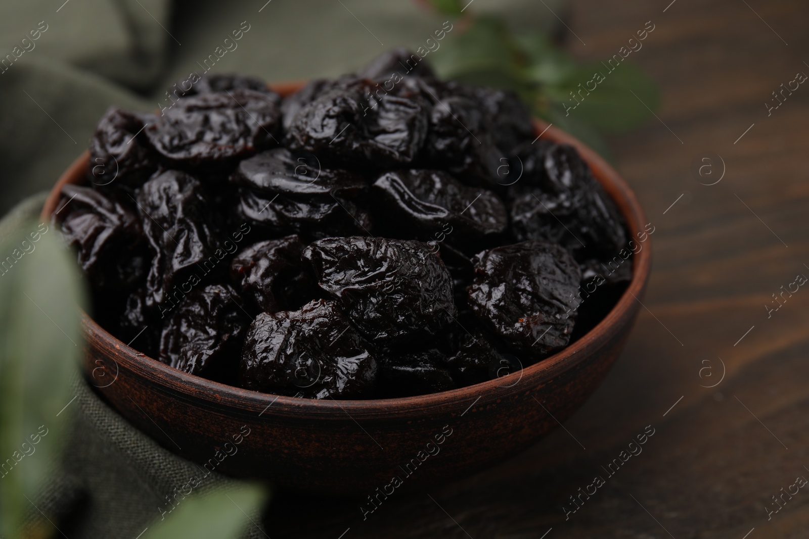 Photo of Sweet dried prunes in bowl on wooden table, closeup