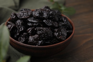 Sweet dried prunes in bowl on wooden table, closeup
