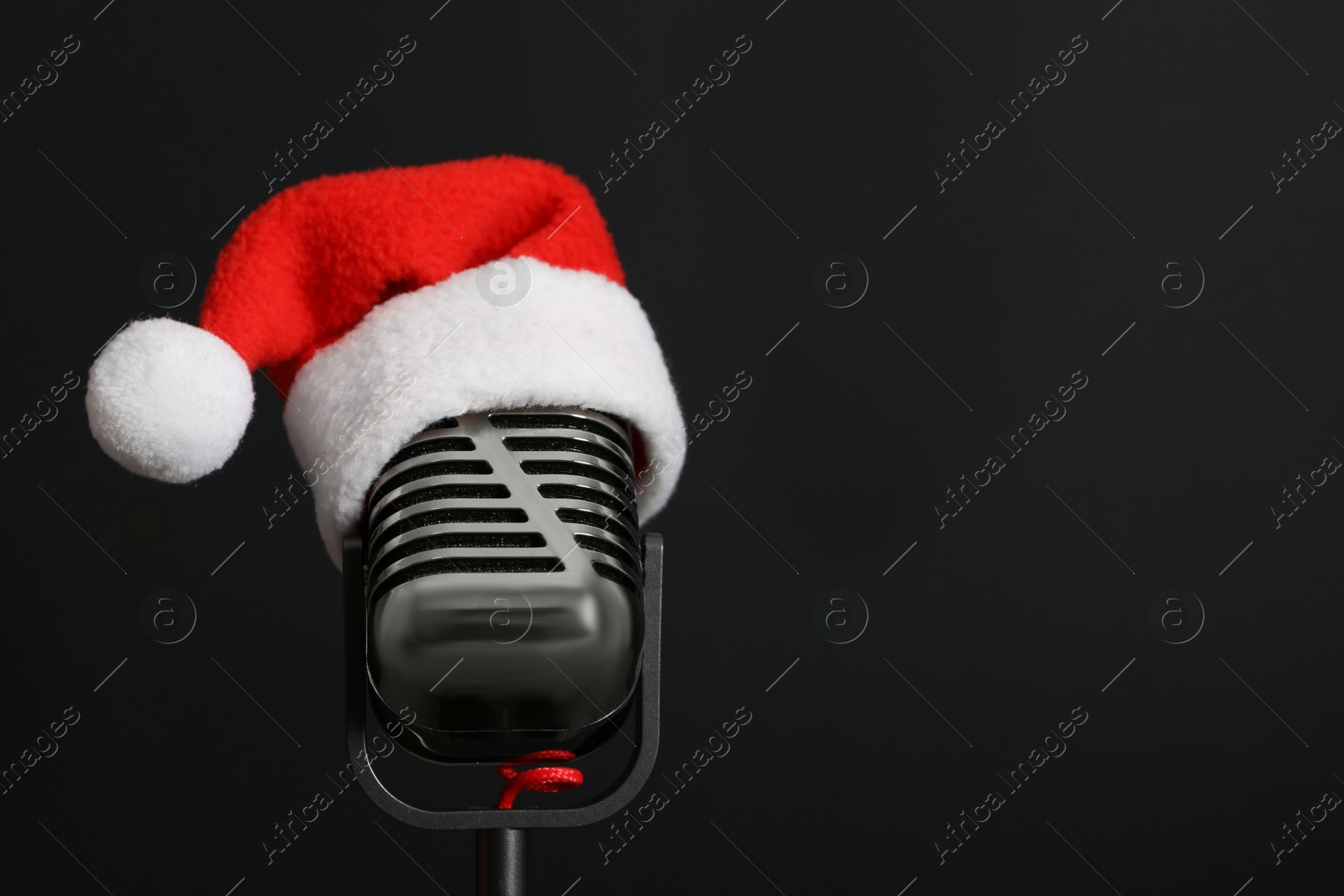 Photo of Retro microphone with Santa hat on black background, space for text. Christmas music