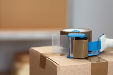 Photo of Adhesive tape dispenser on cardboard box indoors. Space for text
