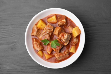 Delicious goulash in bowl on black wooden table, top view