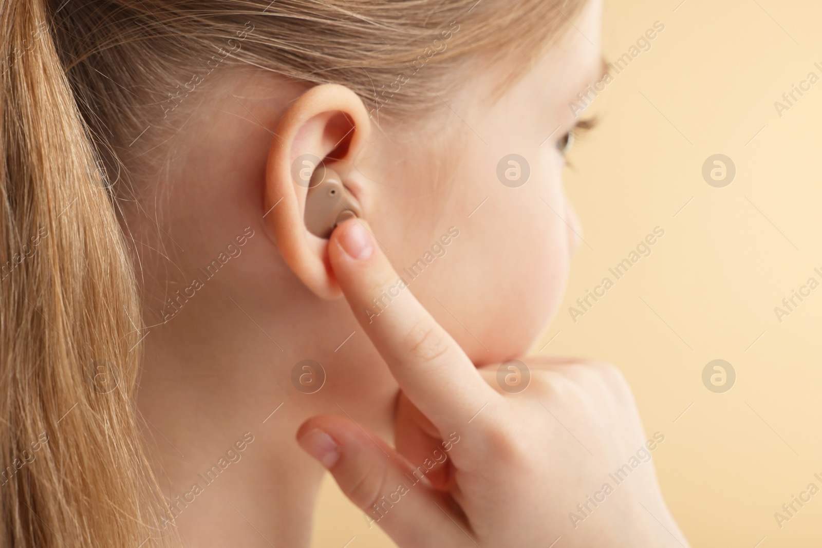 Photo of Little girl with hearing aid on pale brown background, closeup