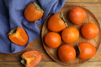 Photo of Tasty ripe persimmons on wooden table, flat lay