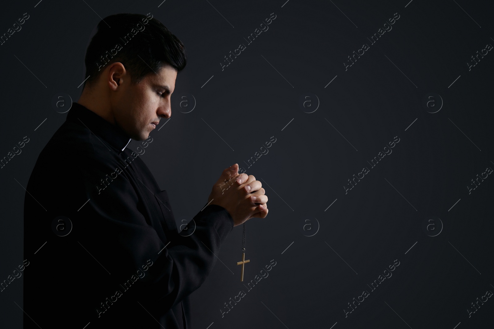 Photo of Priest with cross praying on black background. Space for text