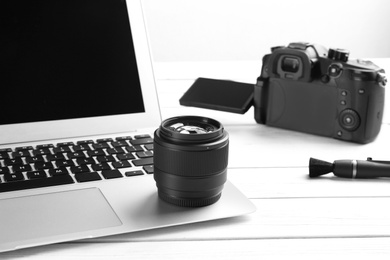 Photo of Modern laptop and camera lens on white wooden table, closeup. Video production industry