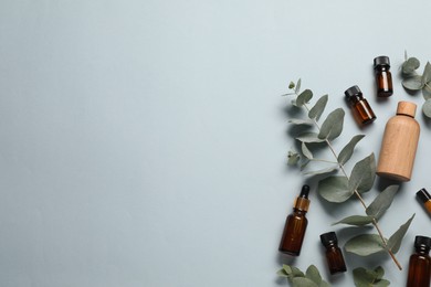 Aromatherapy. Bottles of essential oil and eucalyptus leaves on light grey background, flat lay. Space for text