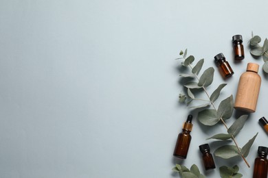 Photo of Aromatherapy. Bottles of essential oil and eucalyptus leaves on light grey background, flat lay. Space for text