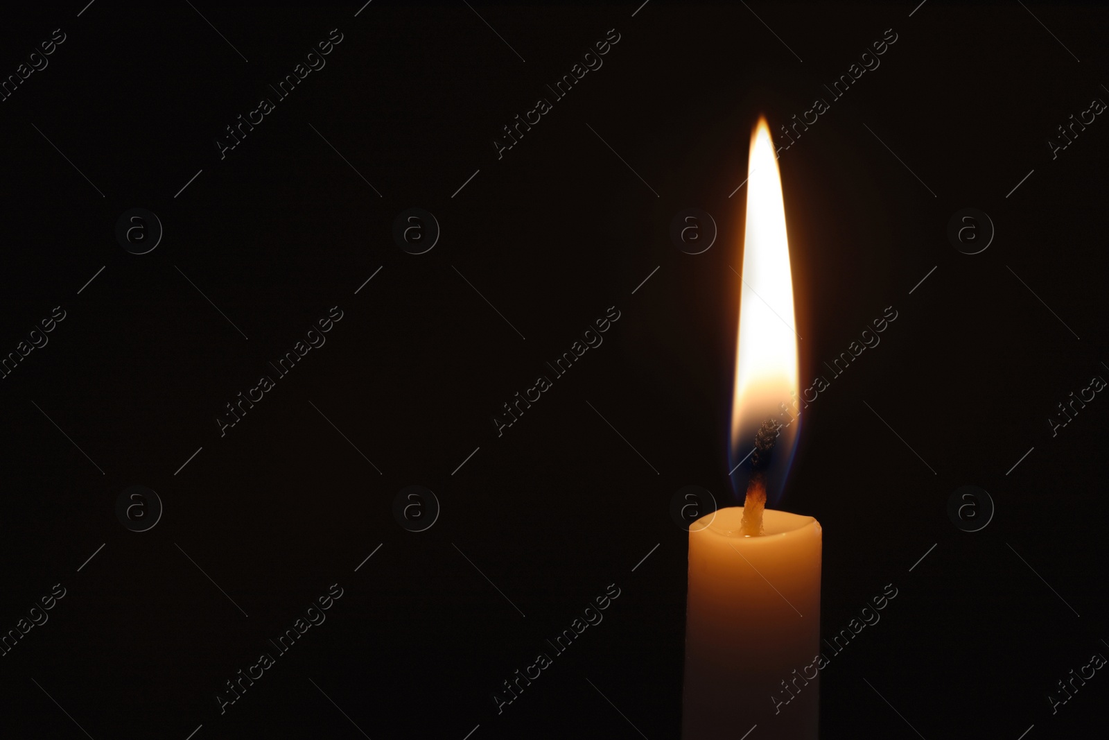 Photo of Wax candle burning on black background, closeup