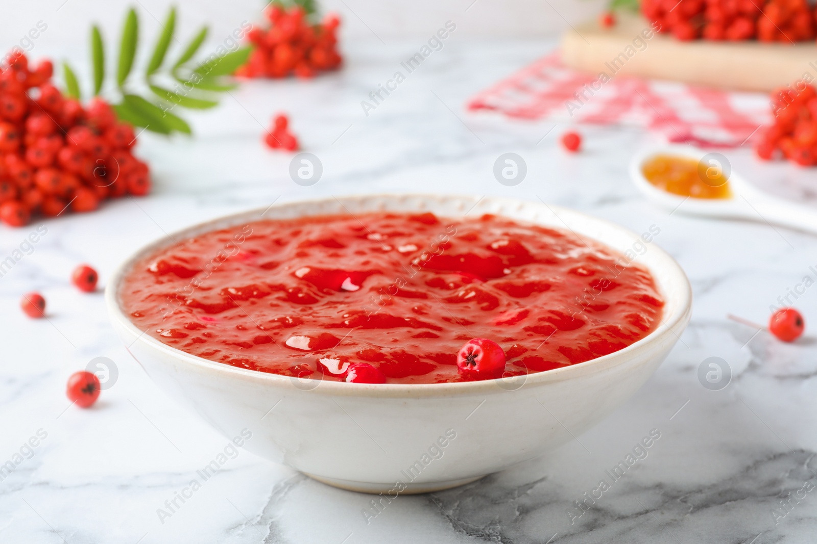 Photo of Delicious rowan jam in bowl and berries on white marble table, closeup