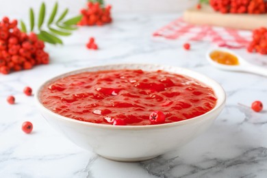 Photo of Delicious rowan jam in bowl and berries on white marble table, closeup