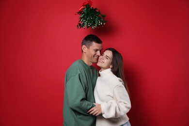 Happy couple standing under mistletoe bunch on red background