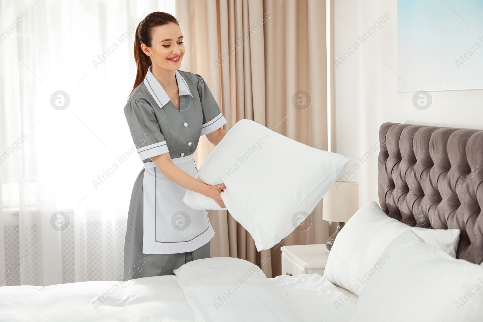 Photo of Young chambermaid making bed in hotel room. Space for text