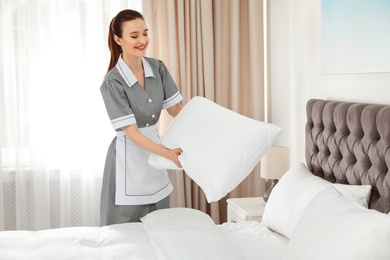 Young chambermaid making bed in hotel room. Space for text