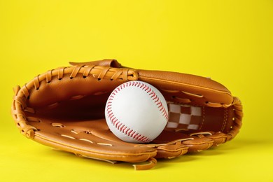 Photo of Catcher's mitt and baseball ball on yellow background. Sports game