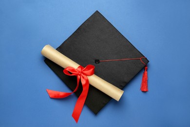 Graduation hat and diploma on blue background, top view