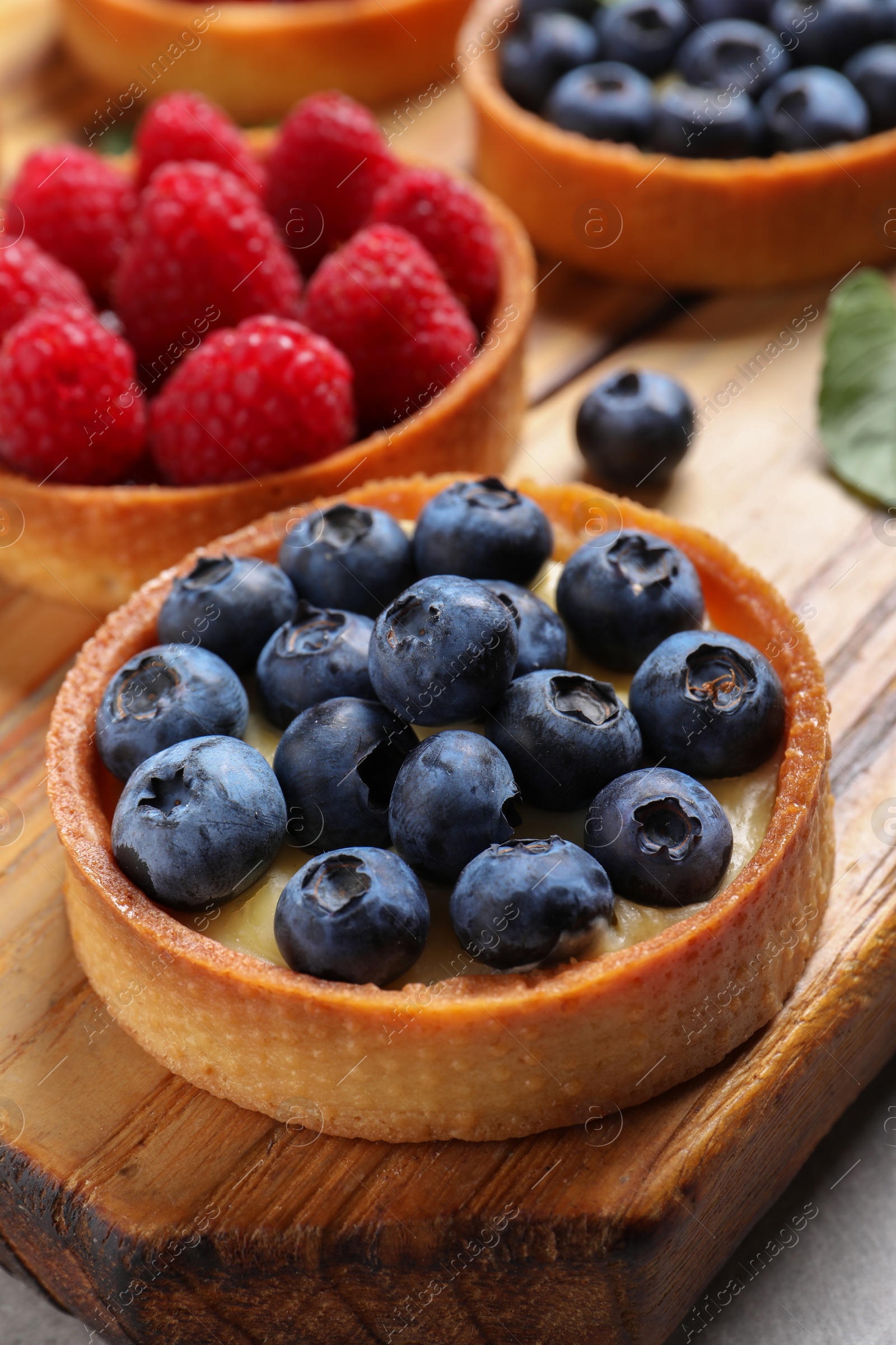 Photo of Tartlet with fresh blueberries on wooden board. Delicious dessert