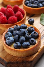 Photo of Tartlet with fresh blueberries on wooden board. Delicious dessert