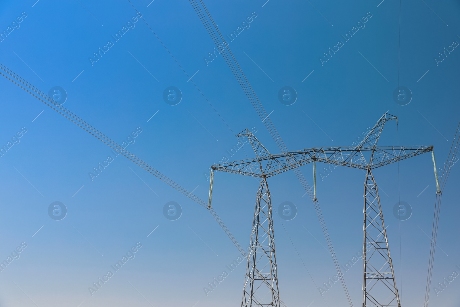 Photo of High voltage tower with electricity transmission power lines against blue sky, low angle view