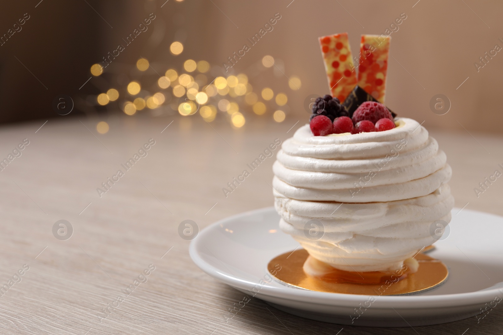 Photo of Delicious meringue dessert with berries on wooden table against blurred lights, closeup. Space for text