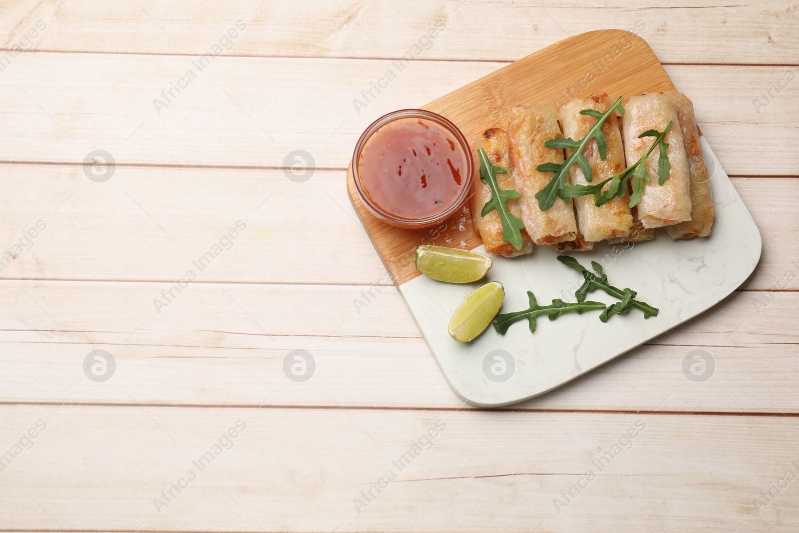 Photo of Tasty fried spring rolls, lime, arugula and sauce on light wooden table, top view. Space for text