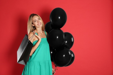 Photo of Happy young woman with balloons and shopping bag on red background. Black Friday Sale