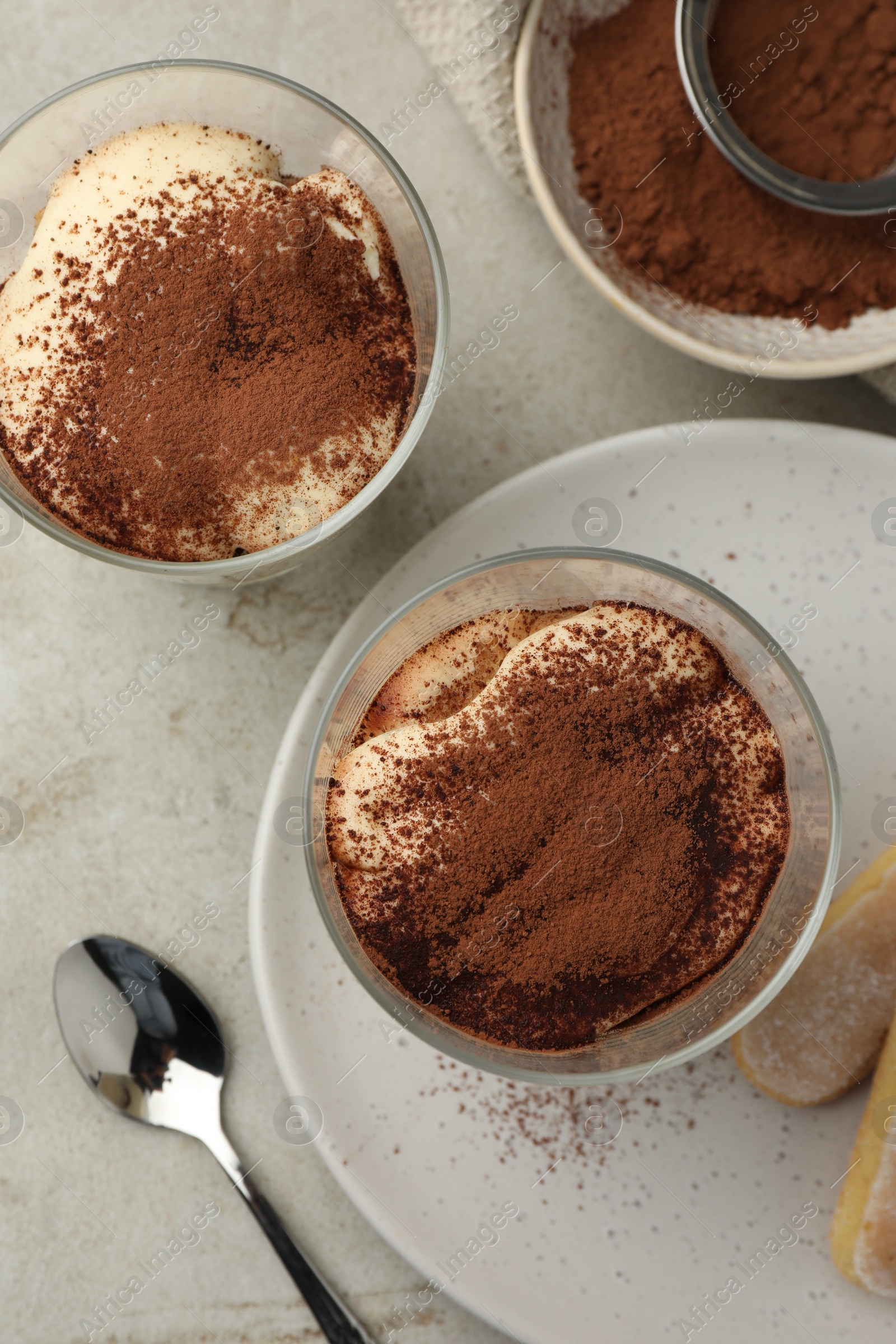 Photo of Delicious tiramisu in glasses, cookies and sieve with cocoa powder on light table, flat lay