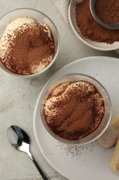 Photo of Delicious tiramisu in glasses, cookies and sieve with cocoa powder on light table, flat lay