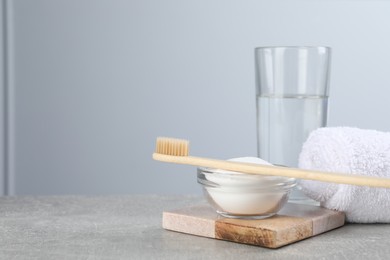 Bamboo toothbrush, bowl of baking soda, towel and glass of water on grey table, space for text