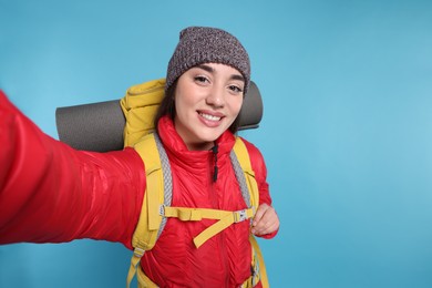 Photo of Smiling young woman with backpack taking selfie on light blue background. Active tourism