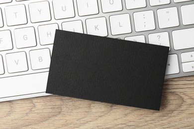 Photo of Blank black business card and computer keyboard on wooden table, top view. Mockup for design